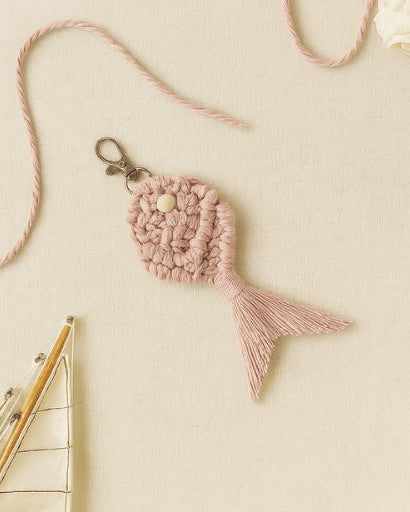 Pastel pink macramé fish keychain displayed on a soft neutral fabric with cotton rope and decorative ship details for a coastal boho look.