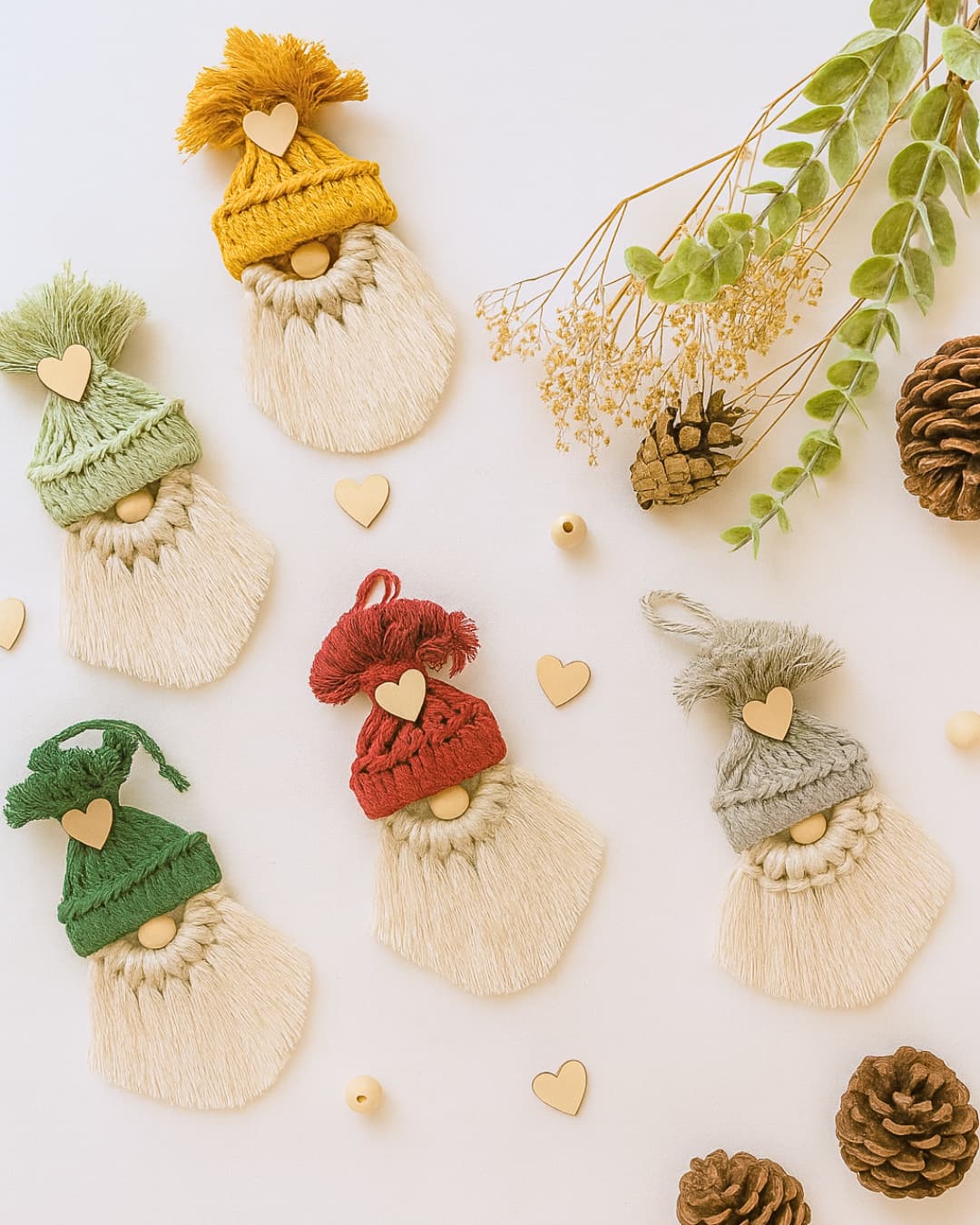 Five handmade macrame gnome Christmas ornaments with cotton beards and wooden hearts, featuring yarn hats in yellow, light green, dark green, red, and grey.