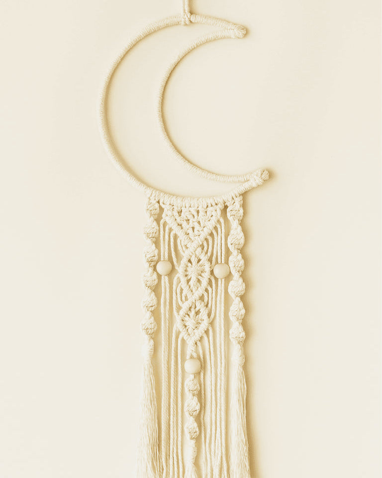 Handmade macramé crescent moon wall hanging with detailed knots and wooden bead accents in off-white cotton cord.