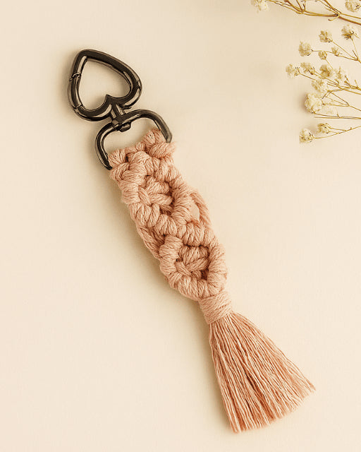 Blush pink macramé diamond keychain with black heart clasp, styled on a soft beige background with dried flowers