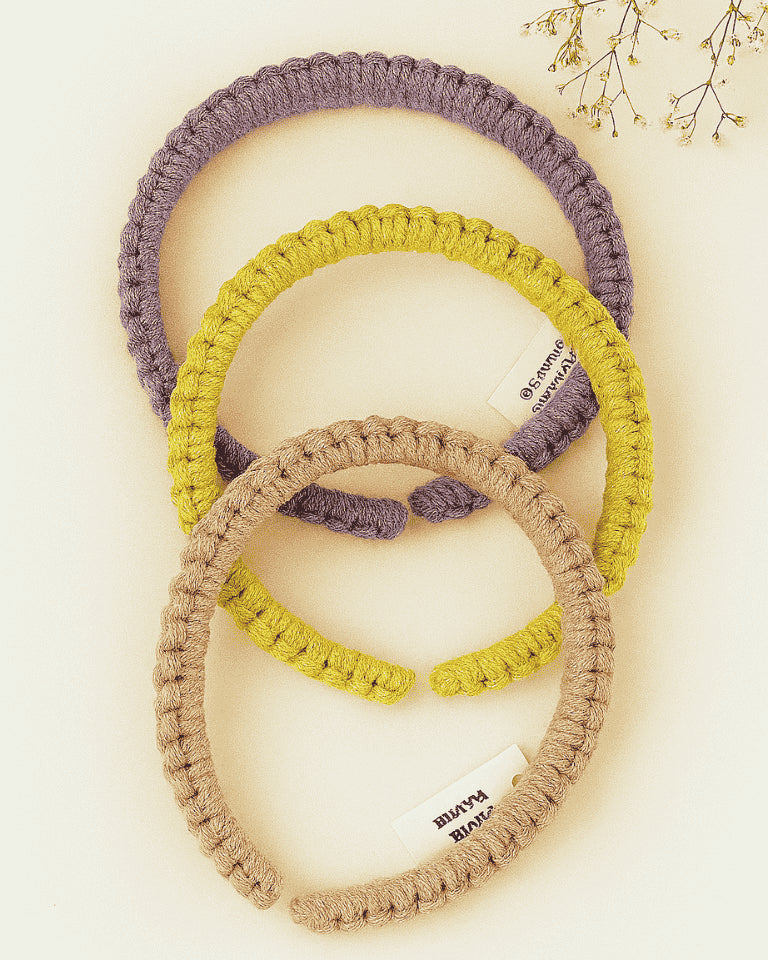Three handmade macramé headbands in lavender, mustard yellow, and blush pink, styled on a neutral background with dried flowers – Samra Knots boho accessory.