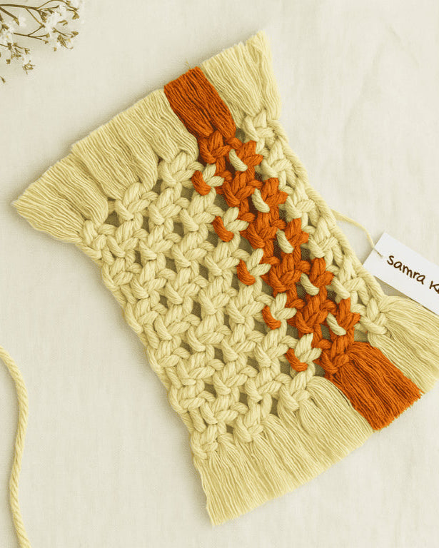 Handmade macramé mug rug in off-white with a terracotta centre stripe, styled on a soft beige linen background – Samra Knots.