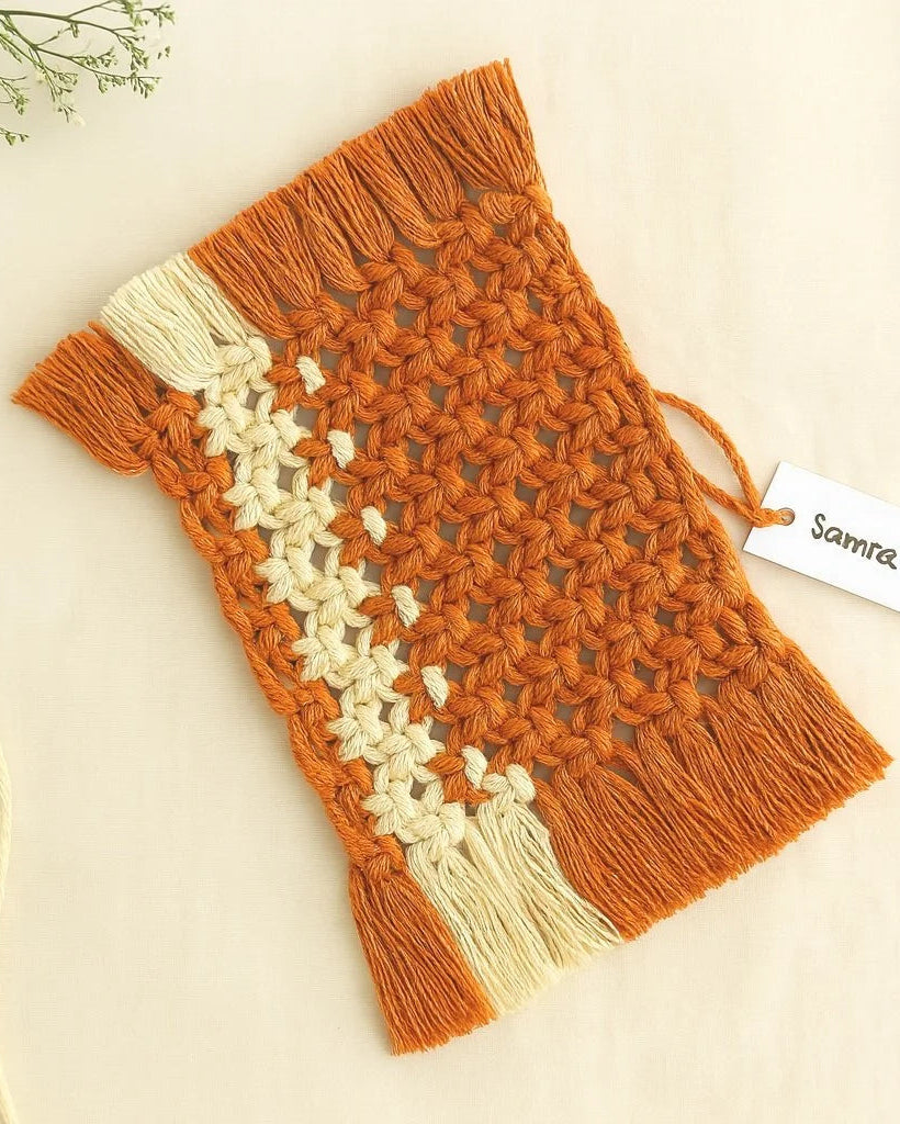 Macramé mug rug in terracotta with a contrasting off-white side stripe, artisan-crafted and laid on a natural linen backdrop – Samra Knots.