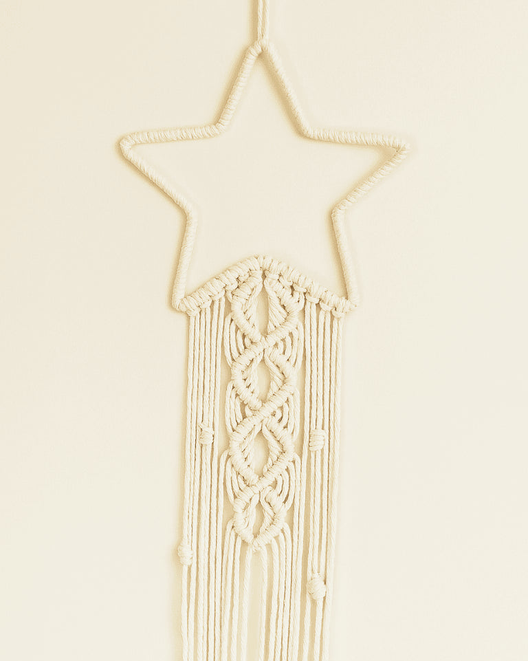 Handmade macramé star wall hanging in off-white cotton cord with elegant knotting and boho fringe design.