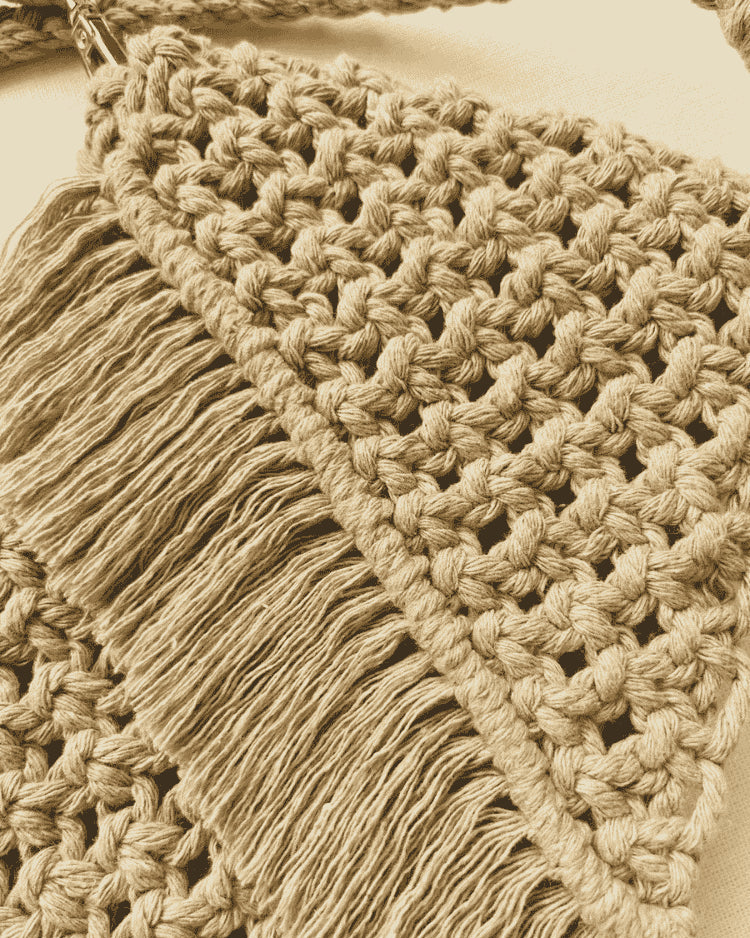 Light brown handmade macramé bag with diagonal fringe and detailed knot pattern, shown flat on an off-white fabric background.