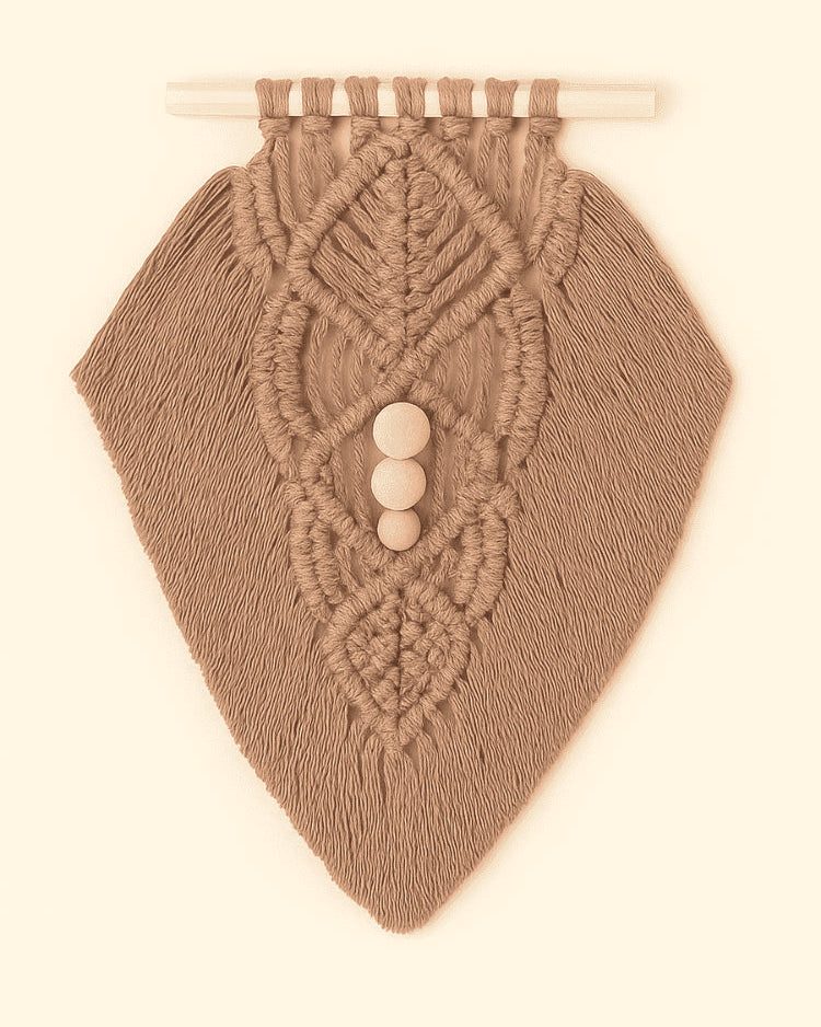 Earthy-toned macramé wall hanging in light brown yarn with detailed knotwork and wooden beads, flat lay style on beige background.