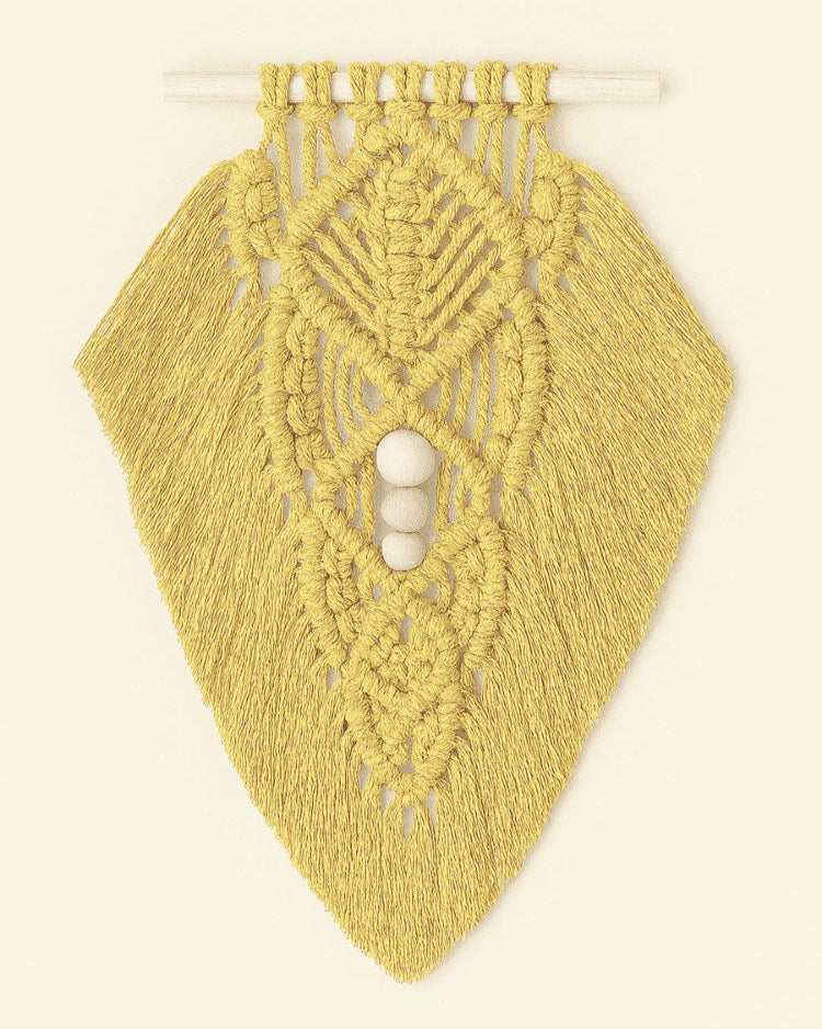 Bright mustard yellow macramé wall hanging with layered leaf pattern and natural wood beads, hanging on light neutral surface.