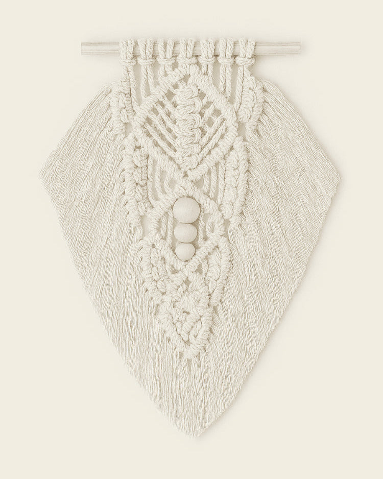 Handmade macramé wall hanging in off-white cotton with intricate leaf pattern and wooden beads, styled on warm beige background.