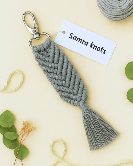 Boho-style grey macramé keychain with a soft beige backdrop, greenery, and tag from Samra Knots.