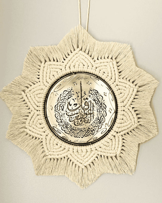 Handmade Islamic wall hanging featuring a gold metal plate with Arabic calligraphy, surrounded by intricate off-white macramé in a starburst pattern