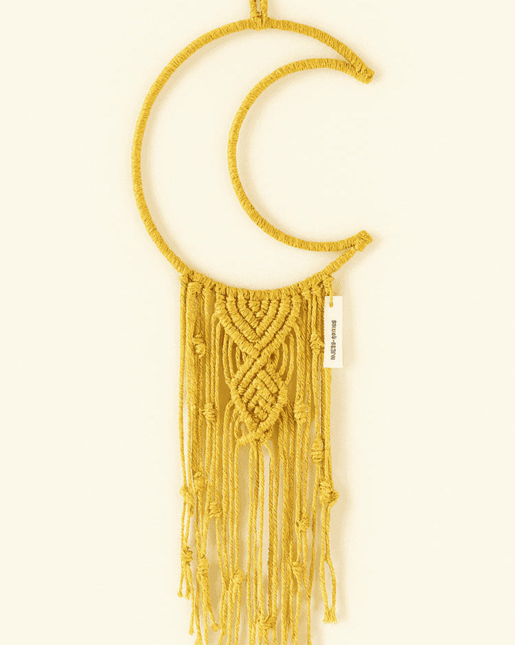 Yellow handmade macramé crescent moon wall hanging with textured twisted knots and long fringe, styled on an off-white background. Bright bohemian home decor.