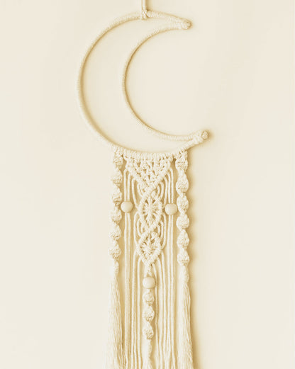 Handmade macramé crescent moon wall hanging with detailed knots and wooden bead accents in off-white cotton cord.