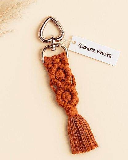 Terracotta handmade macramé keychain with rose gold heart clasp, styled with neutral pampas grass on an off-white background