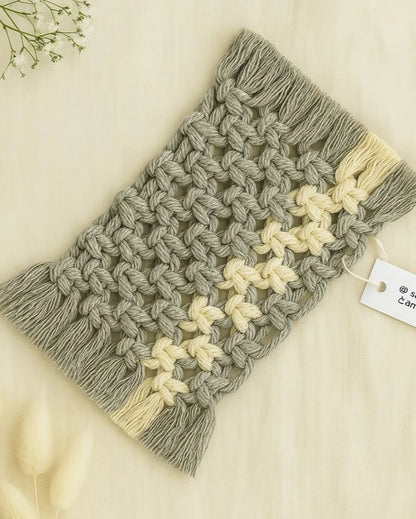 Two-tone macramé mug rug handmade by Samra Knots in grey and off-white, displayed on a soft beige linen background with fluffy dried florals and a product tag for branding.
