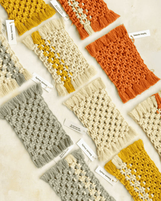 Flatlay of assorted handcrafted macramé mug rugs in earthy tones—grey, mustard yellow, off-white, and terracotta—designed by Samra Knots, arranged on a soft beige surface with brand tags.