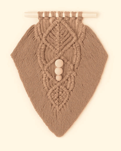 Earthy-toned macramé wall hanging in light brown yarn with detailed knotwork and wooden beads, flat lay style on beige background.