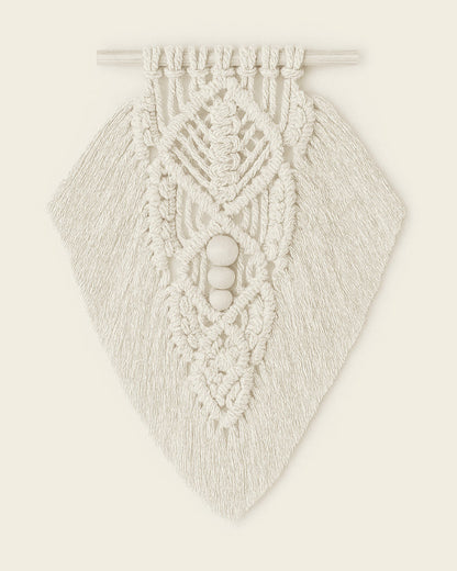 Handmade macramé wall hanging in off-white cotton with intricate leaf pattern and wooden beads, styled on warm beige background.