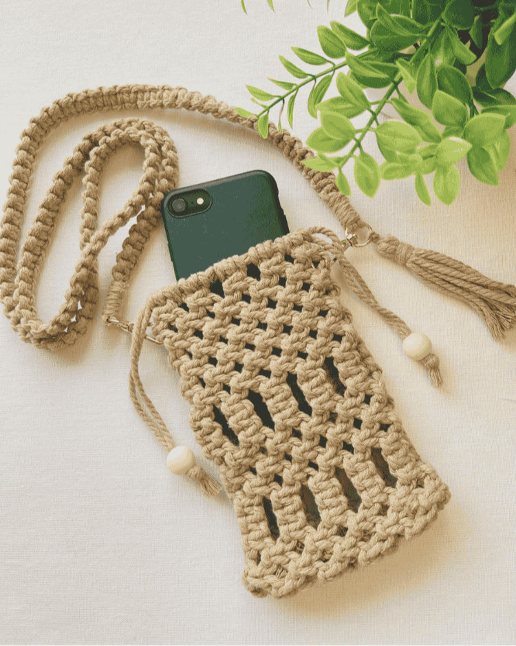 Handmade macramé phone bag in light brown cotton cord with phone inside, styled with braided strap and tassels