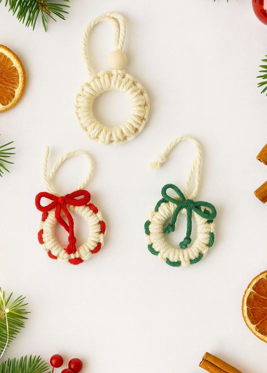 Three handmade mini macramé wreath ornaments in off-white cotton with red, green, and bead details, displayed on an off-white background — eco-friendly Christmas tree decorations.