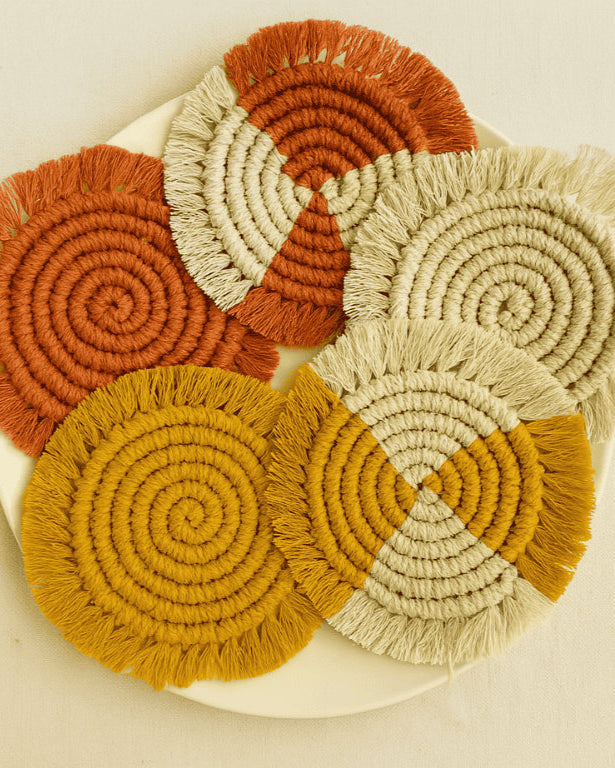 A set of five handcrafted round macramé coasters in terracotta, mustard, and off-white tones, styled on an off-white background. Perfect for boho home decor.